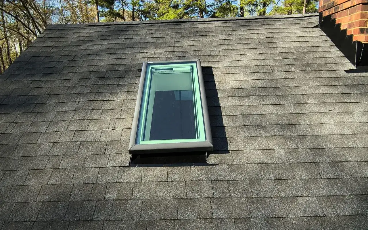 Newly replaced skylight on a dark shingle roof
