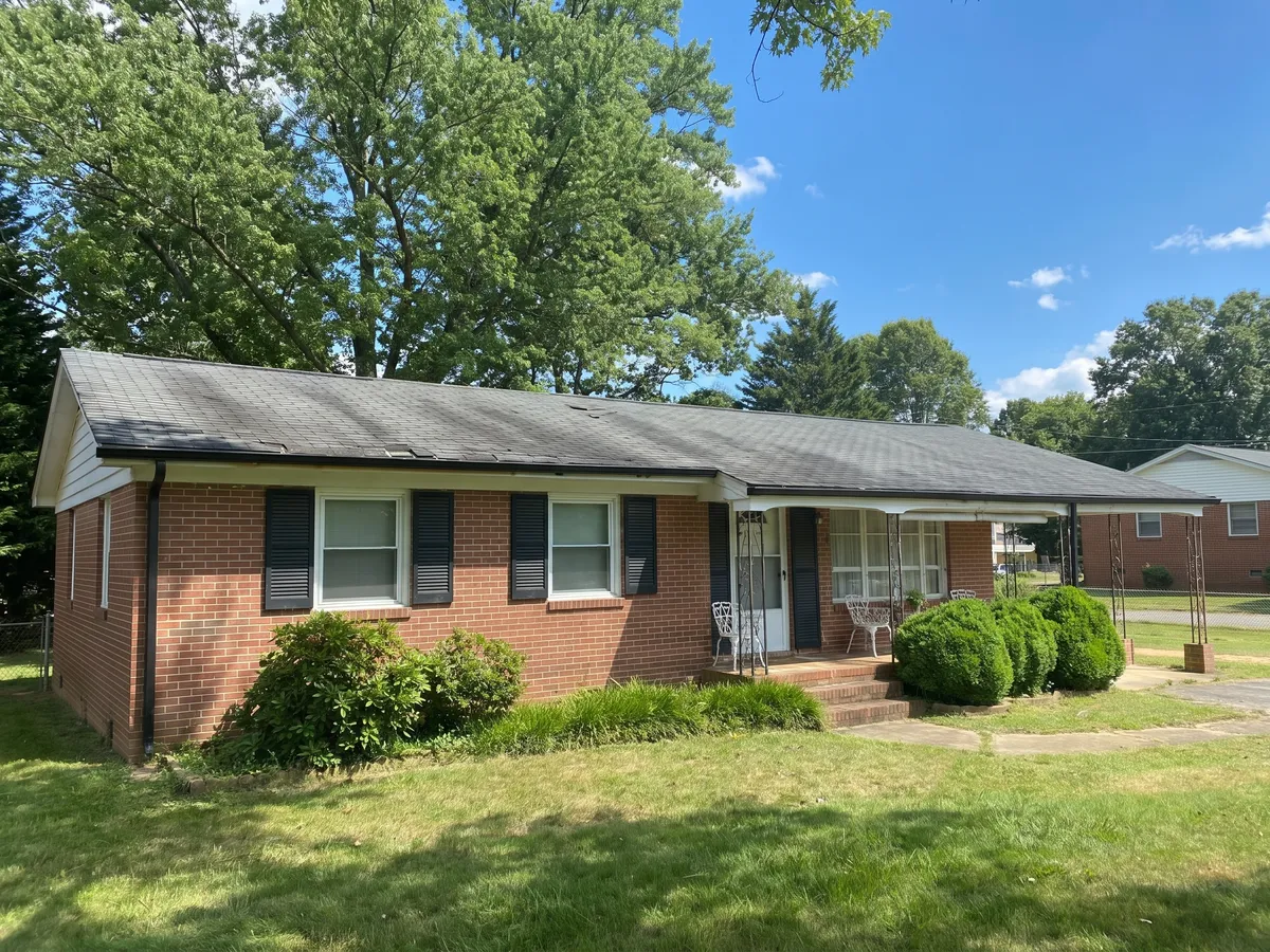 The same brick ranch home before the roof replacement, with a worn and discolored roof
