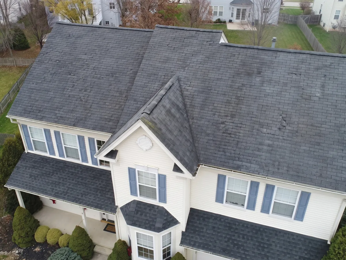The same two-story home before the roof replacement, with an aged and streaked roof